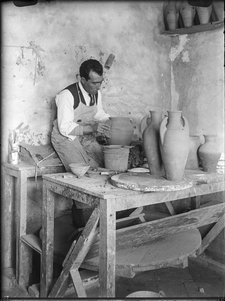 WUNDERLICH (1918-1936) - Forja y alfarería. Alfarero con delantal de trabajo colocando las asas a una vasija. Sobre la mesa, más vasijas