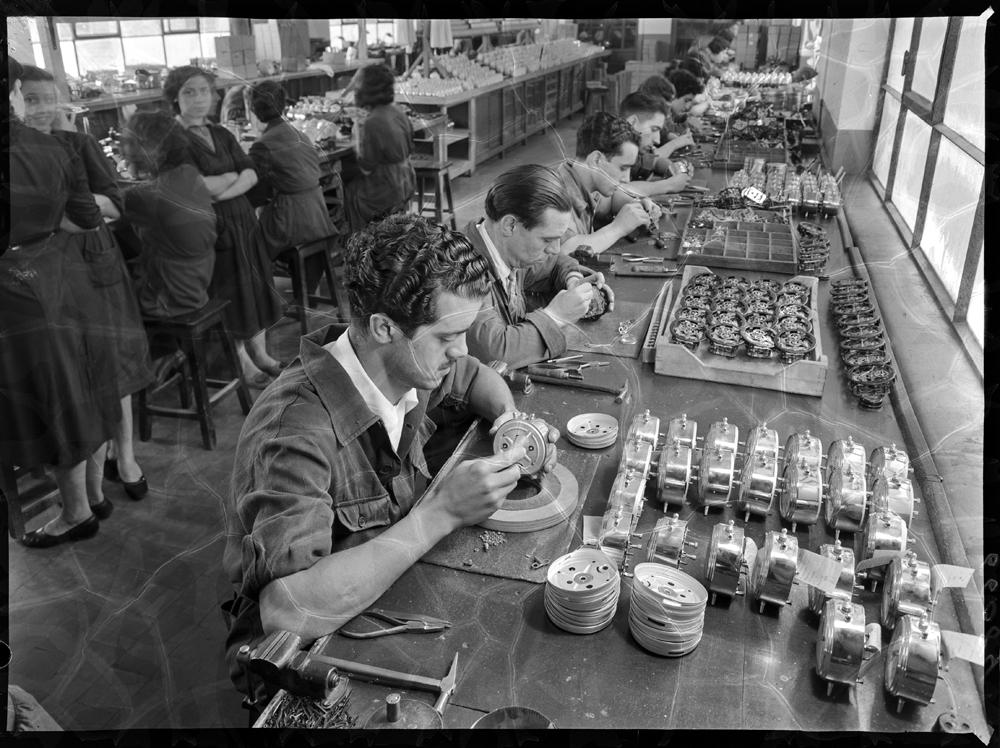 PANDO (1955) - Interior de la fábrica, montando despertadores. Operarios de una fábrica sentados en las mesas de trabajo montando las piezas de un reloj despertador de forma cilíndrica